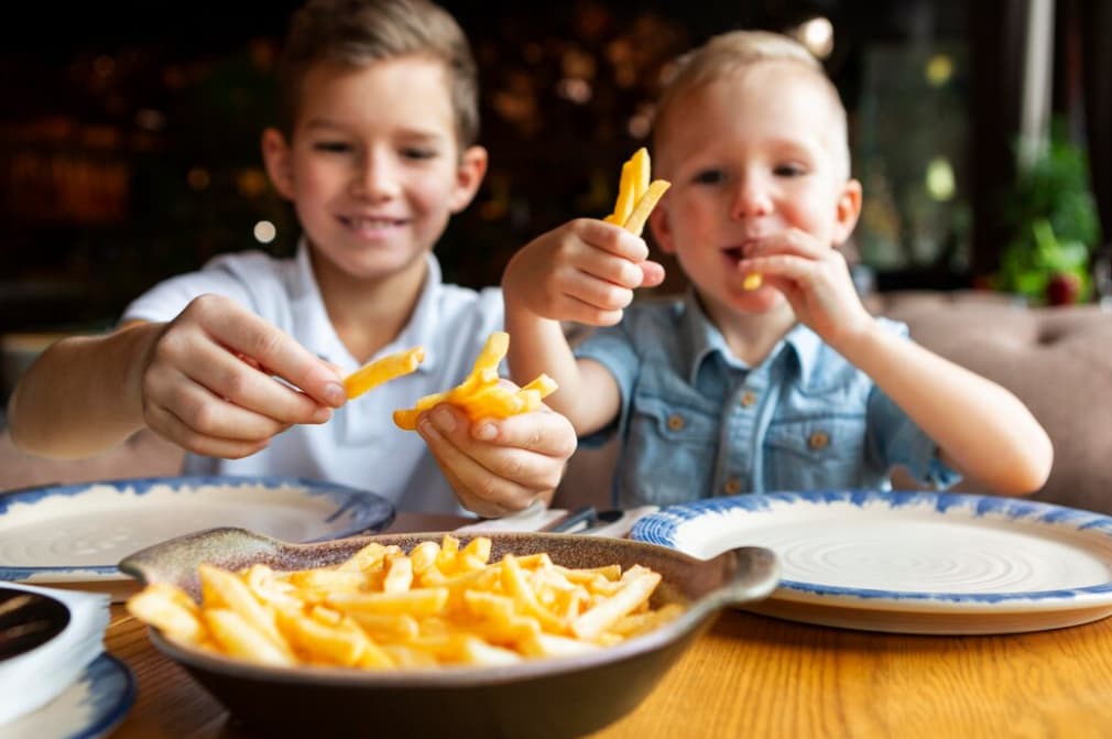 Two children smiling and eating french fries at a restaurant