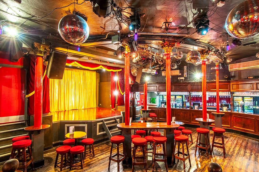 An empty tavern room with red chairs and a stage